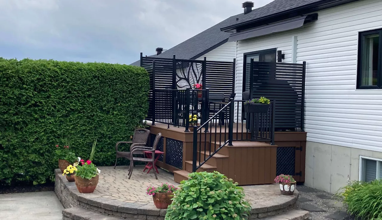 Petit patio avec un plancher en bois et avec clôture et murs d'intimité en aluminium noir, offrant un espace extérieur accueillant et chaleureux.