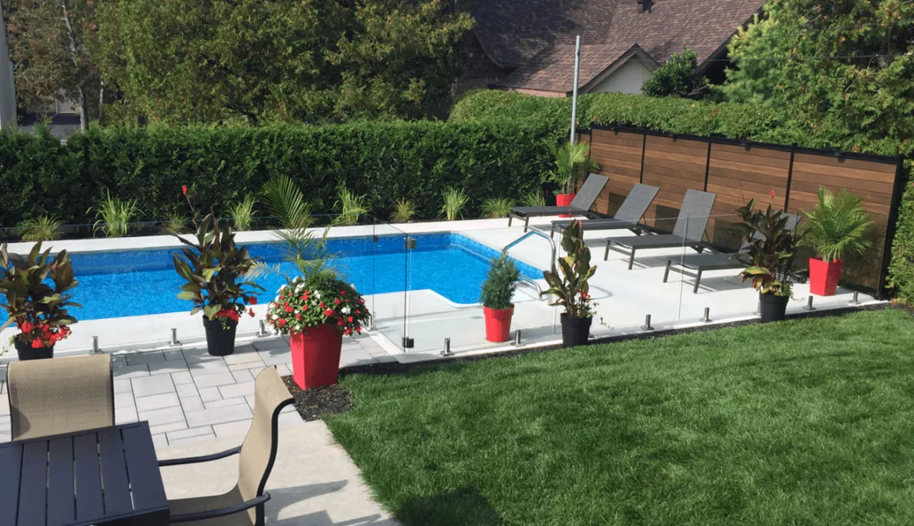 Une cour arrière avec une piscine clôturé avec des panneaux de verre et des meubles de patio, offrant un espace de détente en plein air.