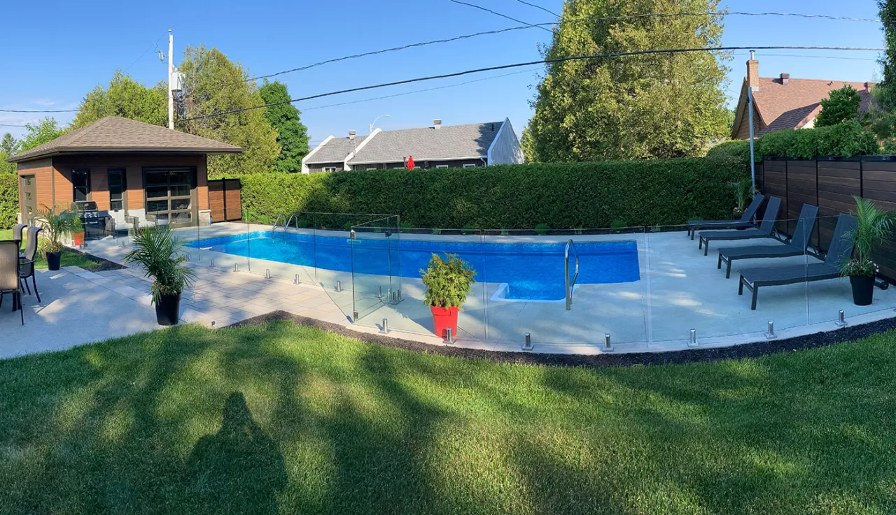 Une piscine dans un jardin avec un grand cabanon muni de portes de garage. Des chaises longues sont installées à l'opposé du cabanon, offrant un espace de détente en plein air.